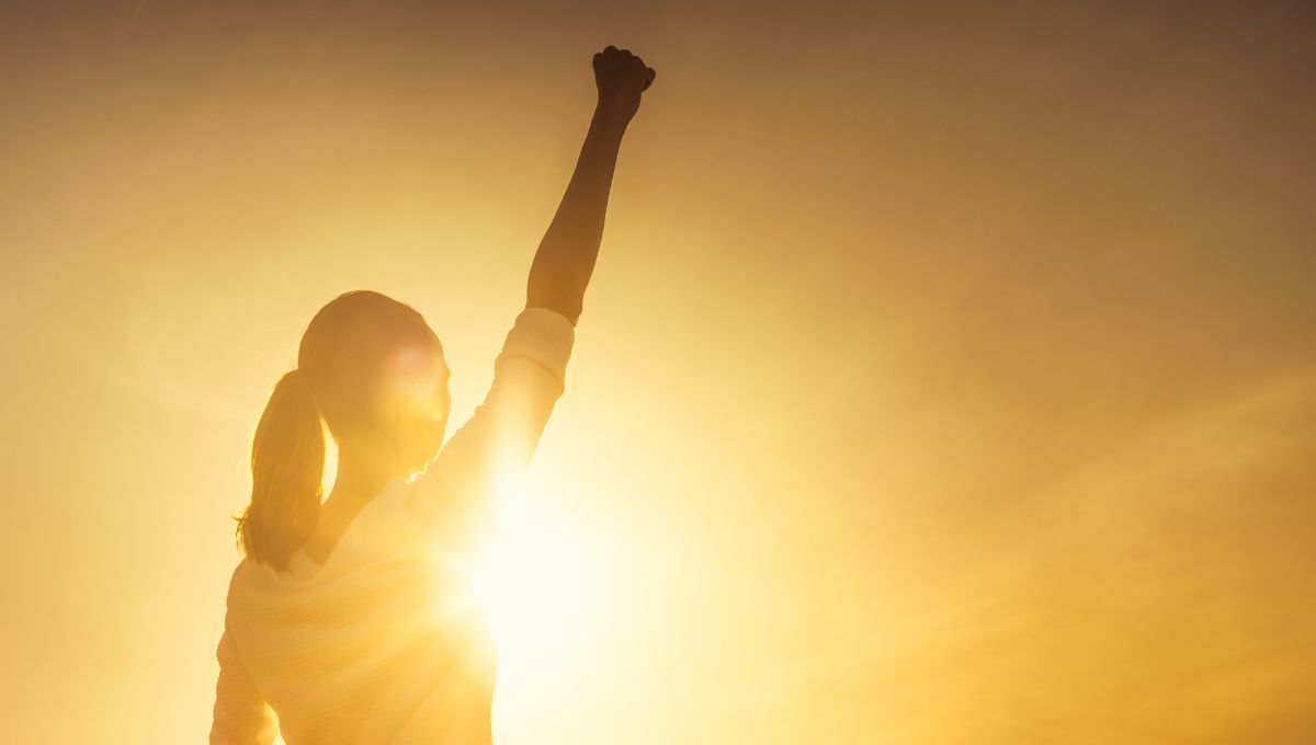 a woman with a pony tail with her fist raised high in victory in front of a sunset a woman with a pony tail with her fist raised high in victory in front of a sunset